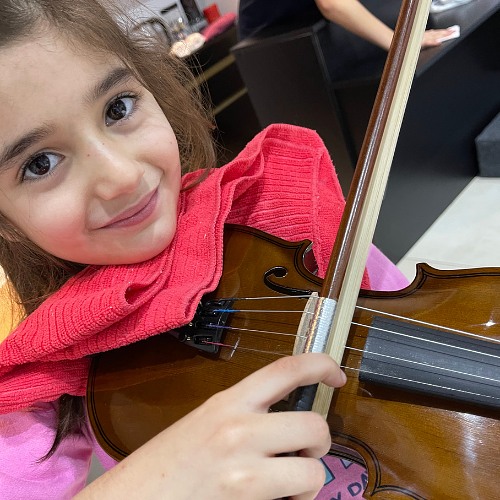 Aluna sorrindo com o violino apoiado no ombro durante a aula