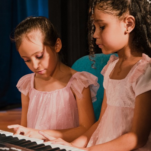 Duas alunas em vestido de apresentação tocando o piano lado a lado