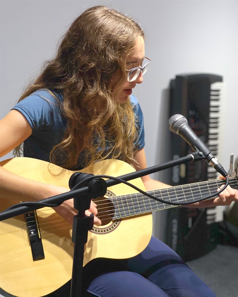 Aluna da Da Capo Musical tocando violão ao microfone durante a aula