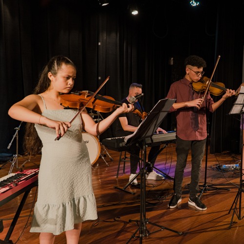 Grupo de alunos tocando violino e violoncelo juntos no palco