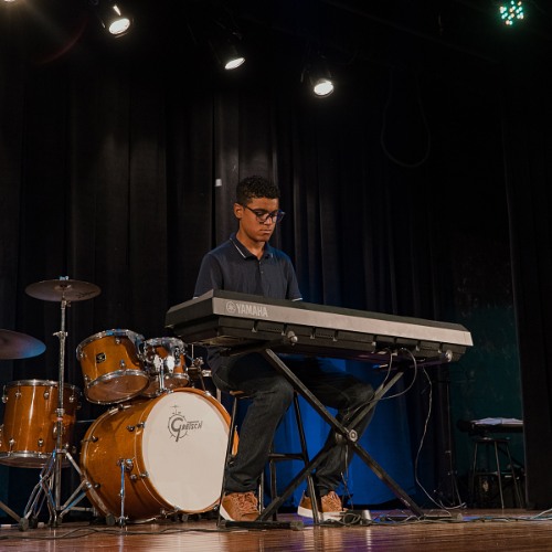 Aluno tocando teclado no palco durante o festival
